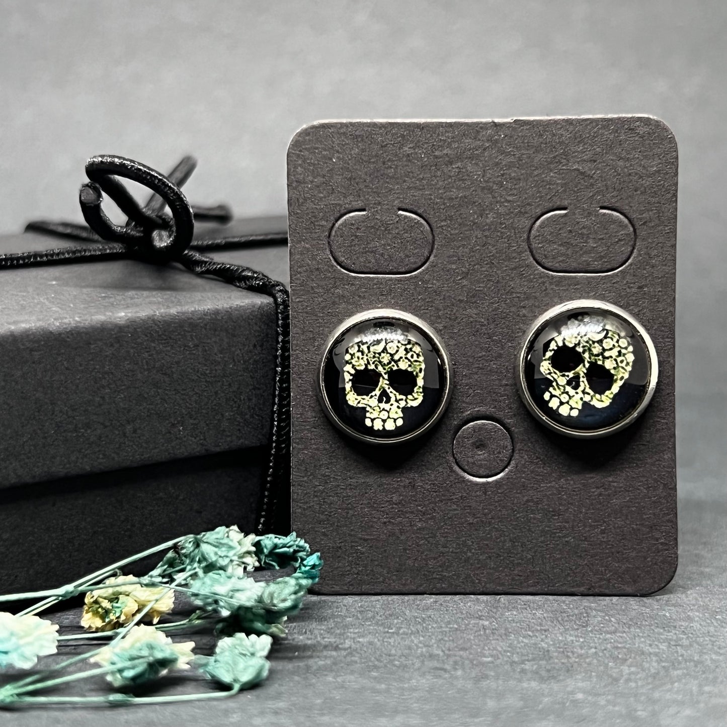 Men's skull stud earrings with dark black and bone color tone designs on silver frame with clear acrylic glass. Man cacochon earrings. Rock, Punk, and Tattoo fashion for man and guys by CALACAMANIA™ accessories.