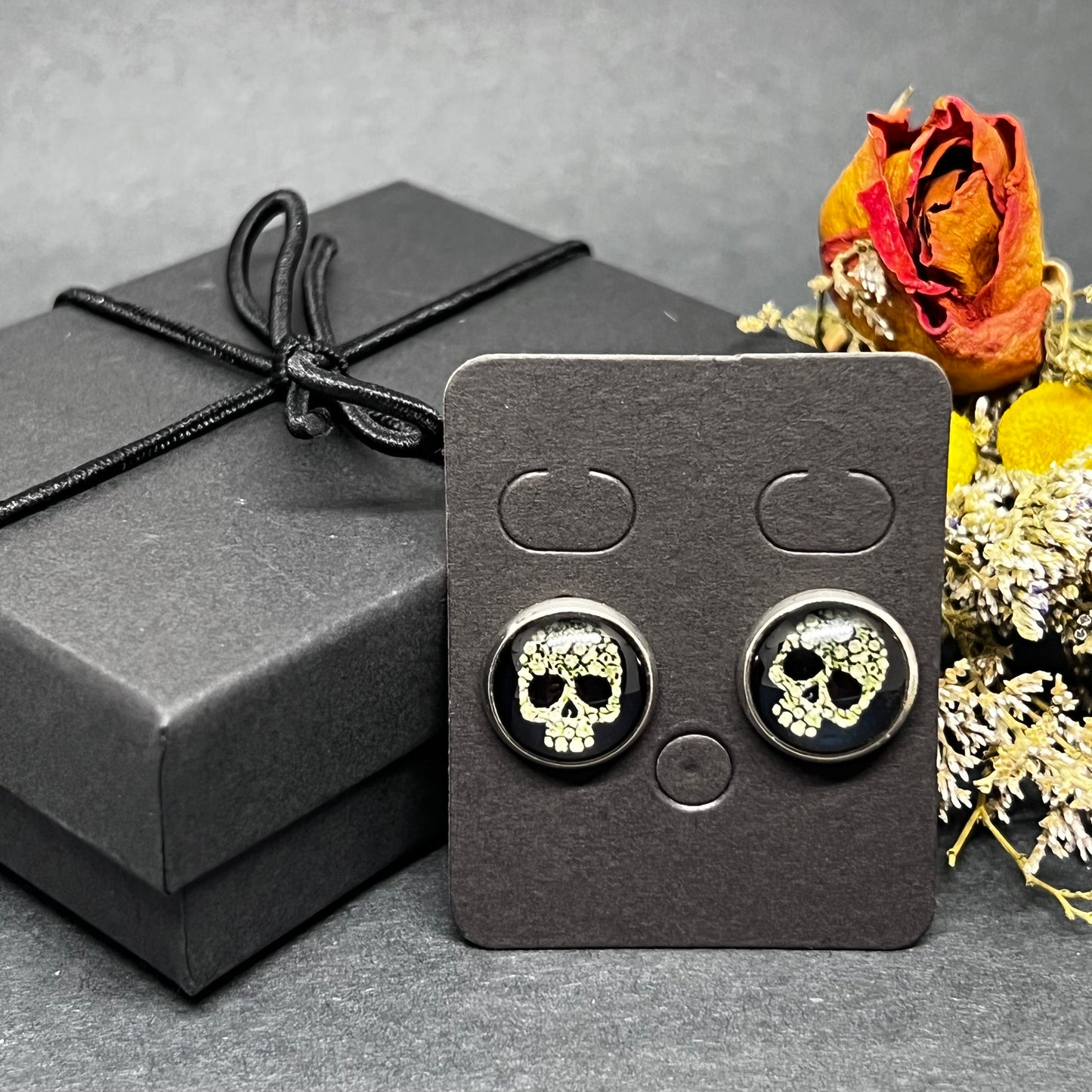 Men's skull stud earrings with dark black and bone color tone designs on silver frame with clear acrylic glass. Man cacochon earrings. Rock, Punk, and Tattoo fashion for man and guys by CALACAMANIA™ accessories.