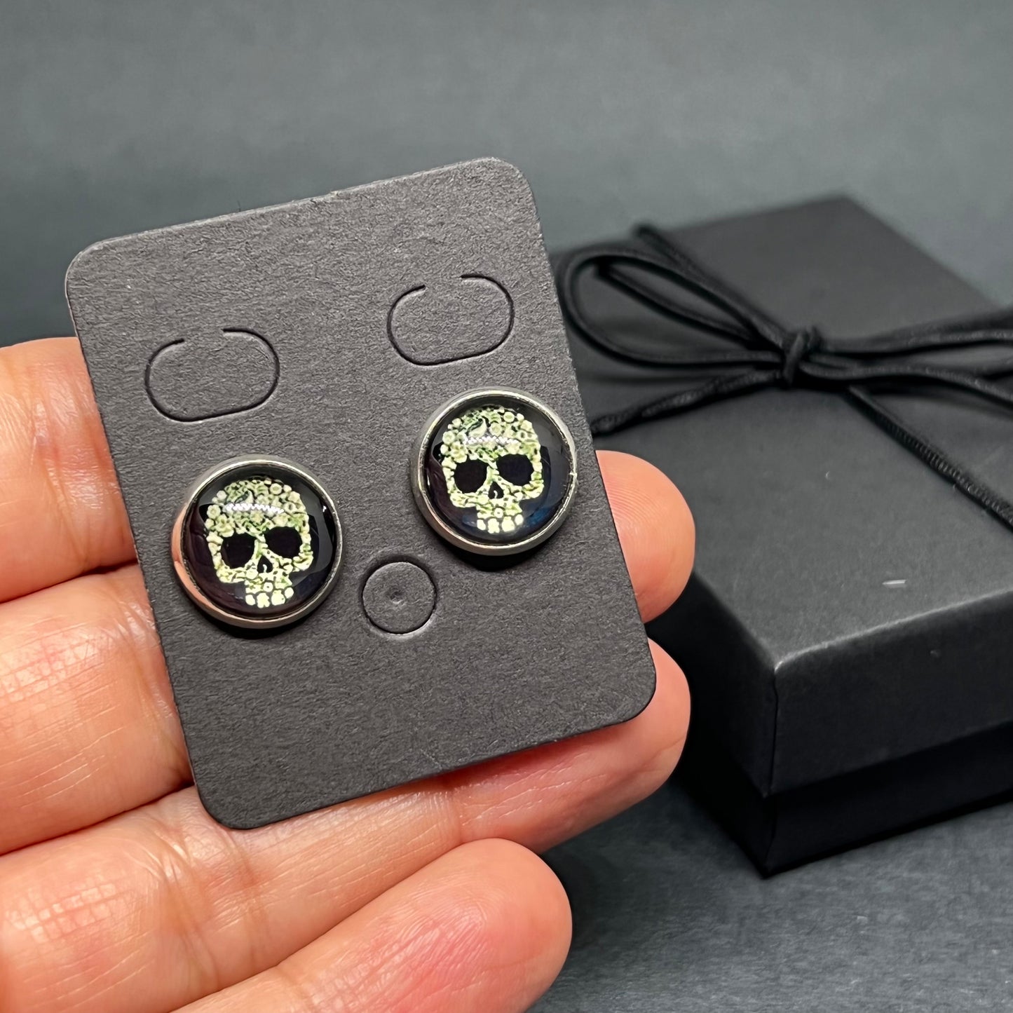 Men's skull stud earrings with dark black and bone color tone designs on silver frame with clear acrylic glass. Man cacochon earrings. Rock, Punk, and Tattoo fashion for man and guys by CALACAMANIA™ accessories.