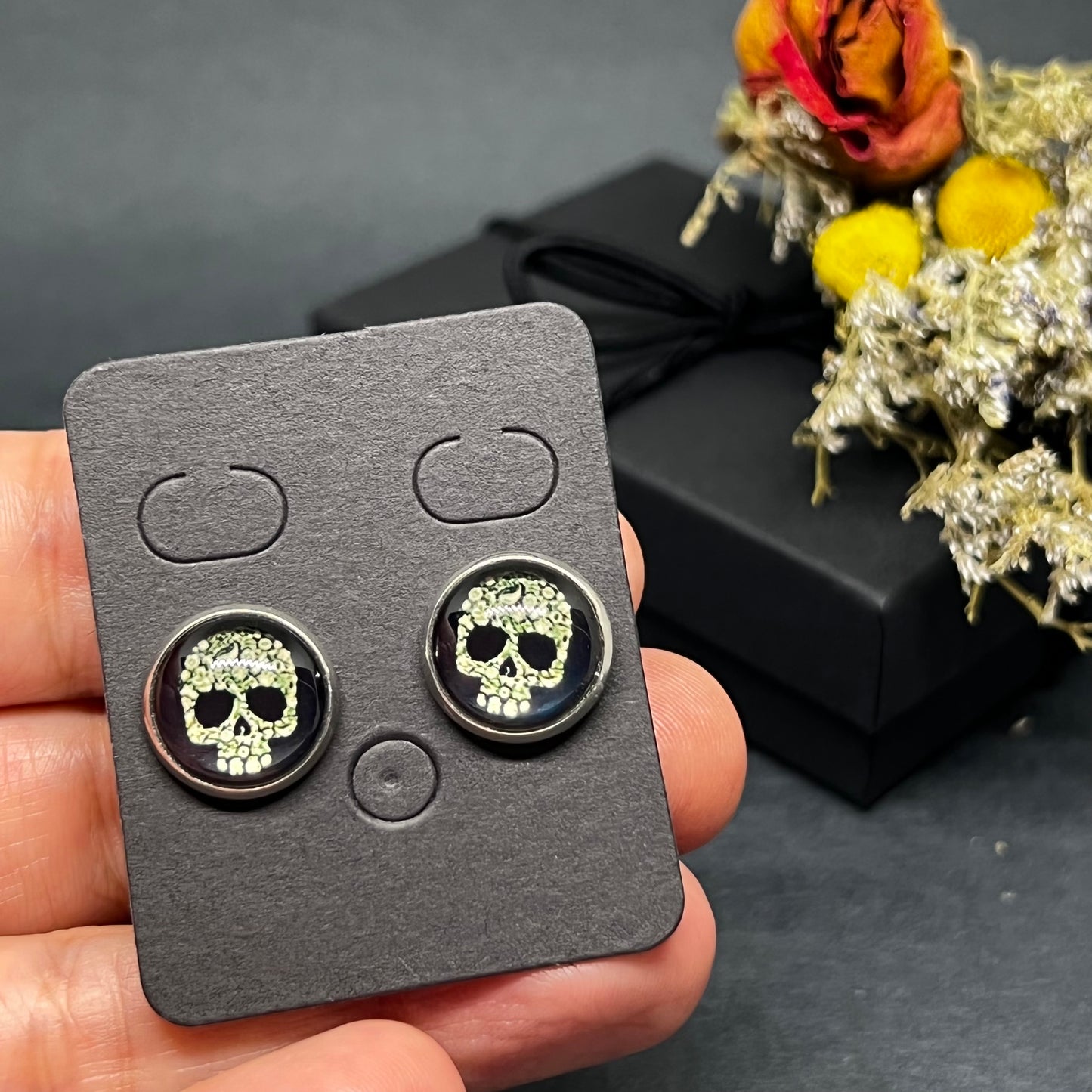 Men's skull stud earrings with dark black and bone color tone designs on silver frame with clear acrylic glass. Man cacochon earrings. Rock, Punk, and Tattoo fashion for man and guys by CALACAMANIA™ accessories.