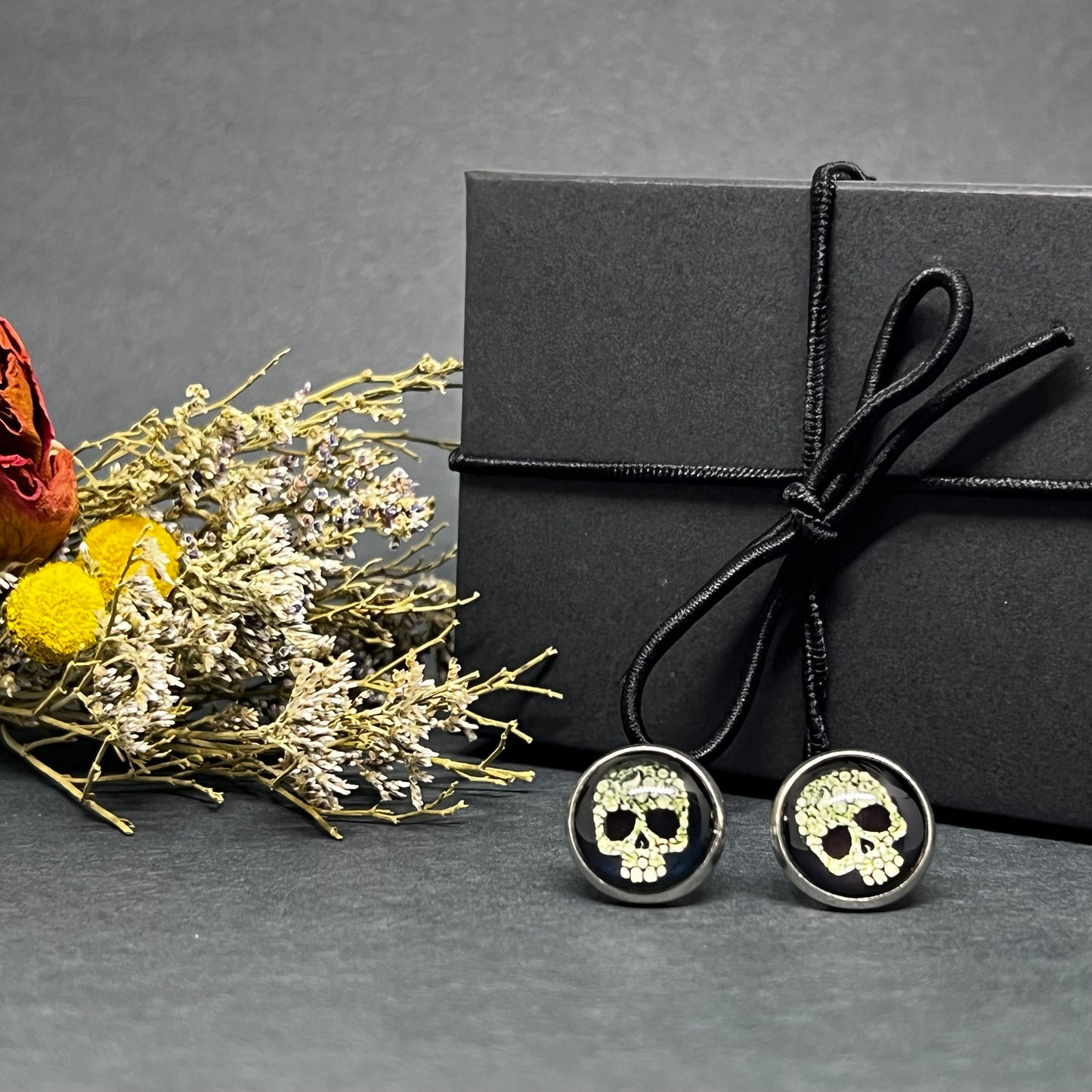 Men's skull stud earrings with dark black and bone color tone designs on silver frame with clear acrylic glass. Man cacochon earrings. Rock, Punk, and Tattoo fashion for man and guys by CALACAMANIA™ accessories.