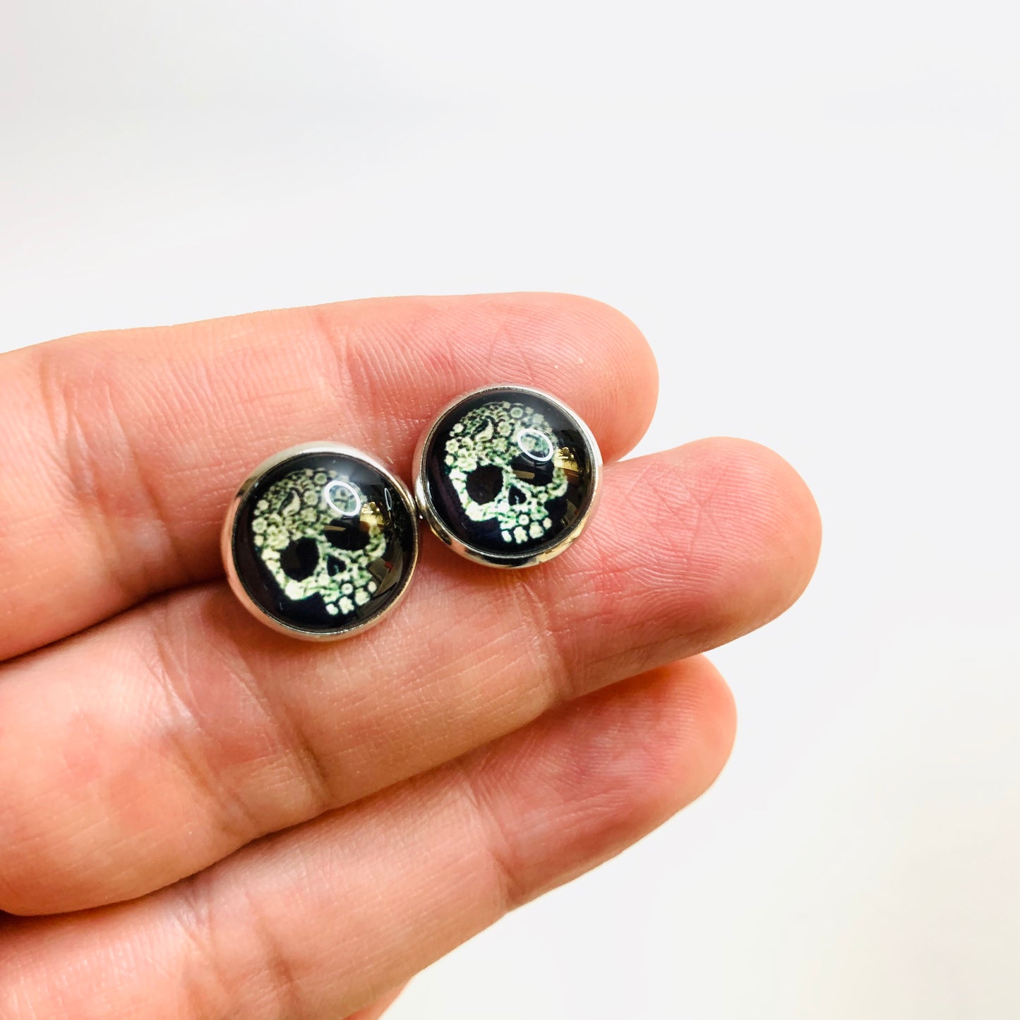 Men's skull stud earrings with dark black and bone color tone designs on silver frame with clear acrylic glass. Man cacochon earrings. Rock, Punk, and Tattoo fashion for man and guys by CALACAMANIA™ accessories.