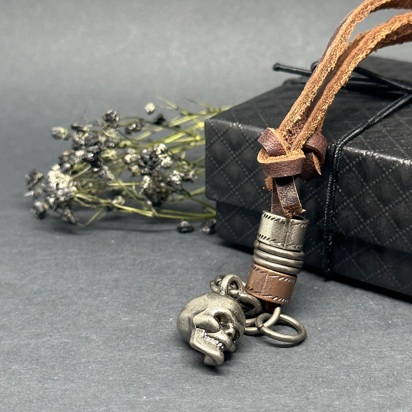 Metallic skull pendant charm with stainless stain rings and disk. Brown leather necklace cord for guys.