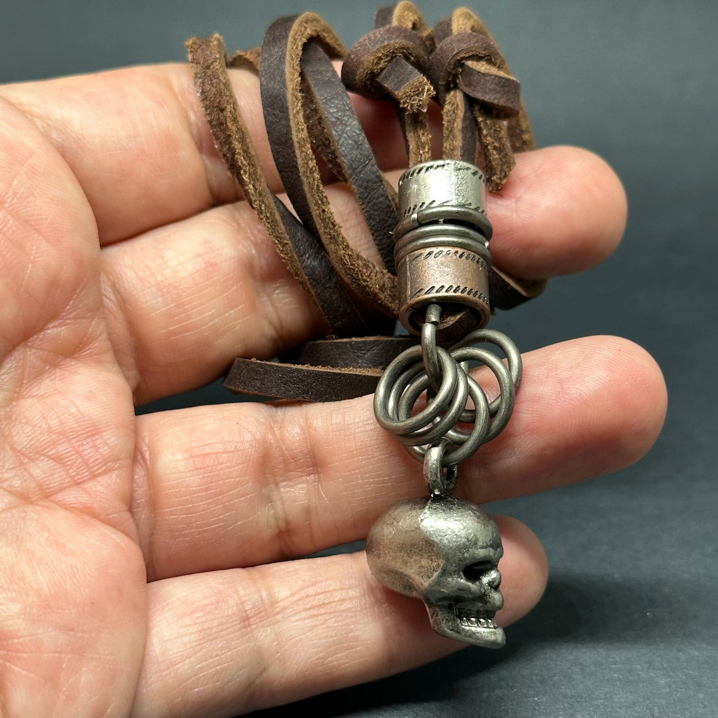 Metallic skull pendant charm with stainless stain rings and disk. Brown leather necklace cord for guys.