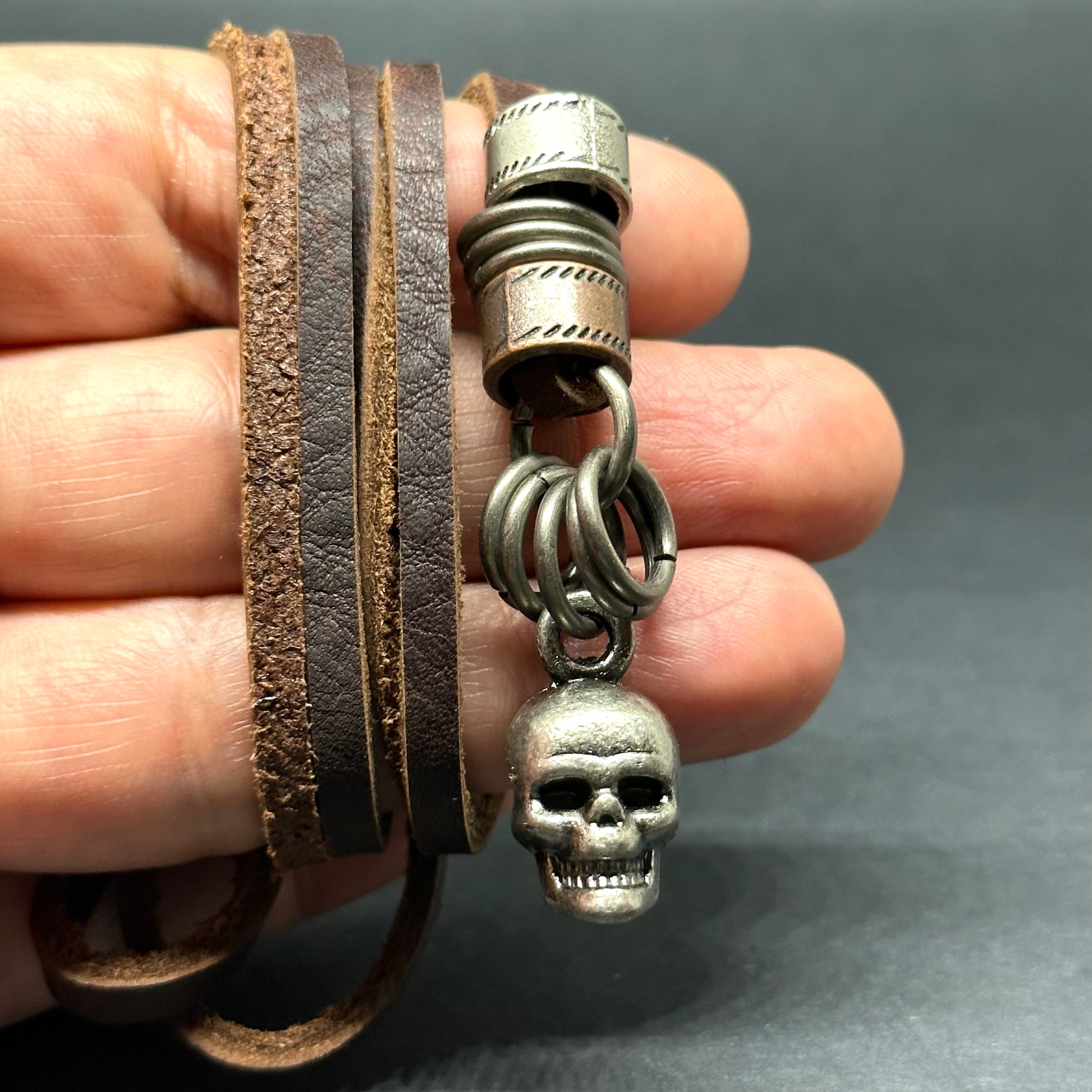 Metallic skull pendant charm with stainless stain rings and disk. Brown leather necklace cord for guys.