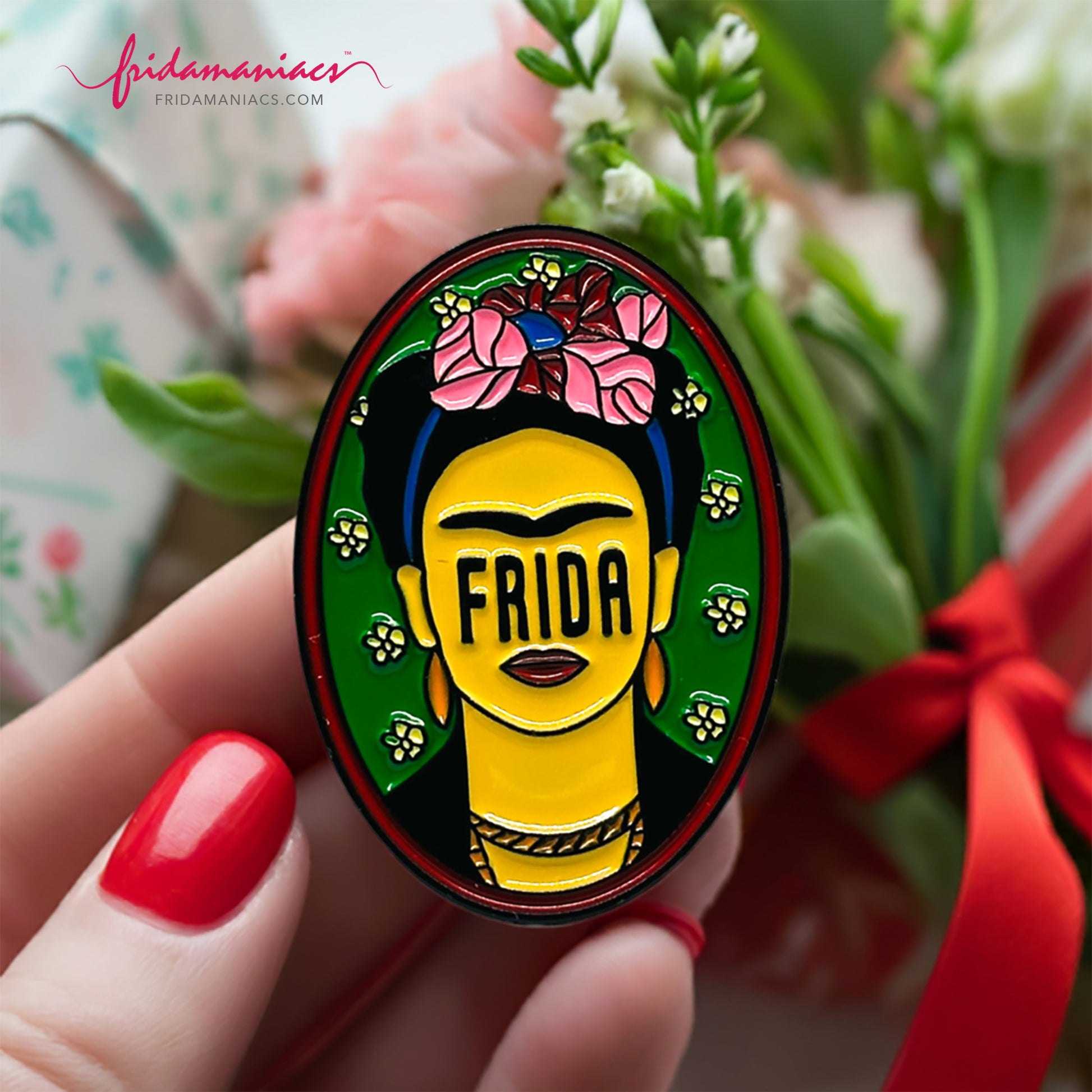 Frida Kahlo oval enamel pin back button with green enamel as background, wine tone frame, and FRIDA spelling instead of eyes below iconic artist eyebrows with pink flowers. Fridamaniacs. Mexican jewelry.