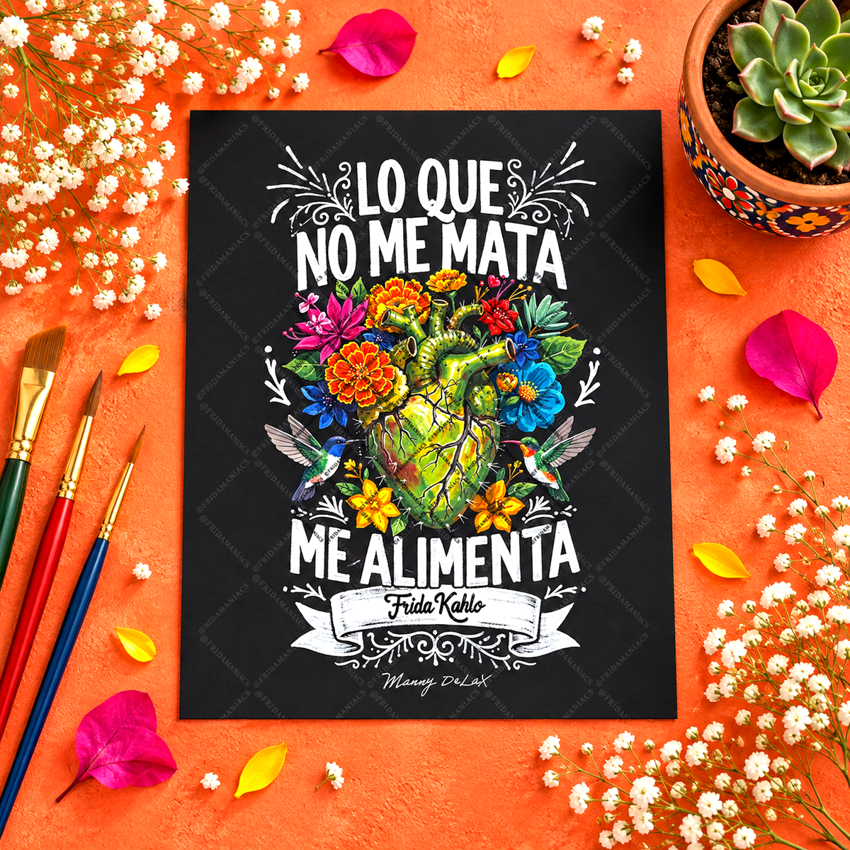 A square black art print with a colorful illustrated heart and flowers, surrounded by white text reading 'LO QUE NO ME MATA ME ALIMENTA' and 'Frida Nobile'. The print is photographed from above on a textured orange surface with scattered white flowers, paintbrushes, petals, and a small potted succulent.