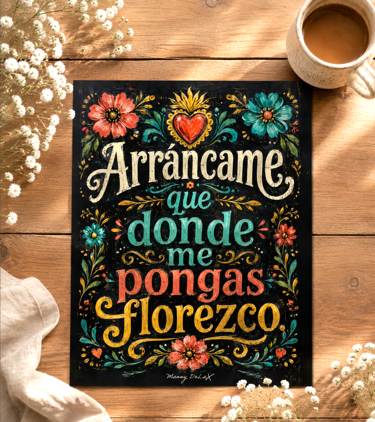 A decorative printed sign or poster with colorful hand-lettered text reading 'Arrancame que donde me pongas floresco' on a black background, styled on a wooden surface with flowers, a cup of coffee, and a cloth.