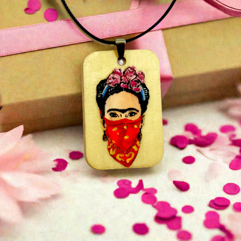 Frida-inspired necklace with a rectangular pendant depicting a woman wearing pink flowers and a red bandana, suspended from a black cord.