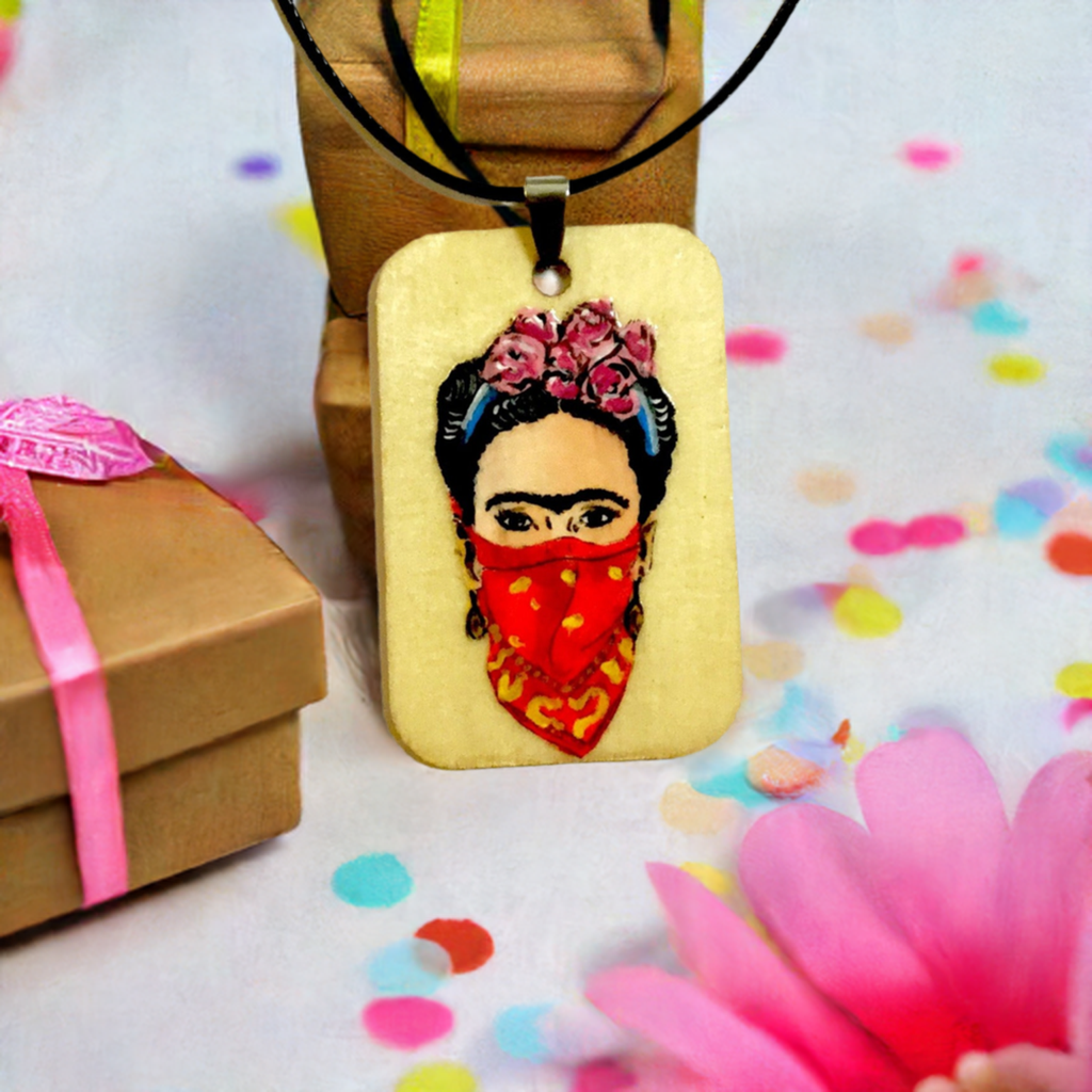 Frida-inspired necklace with a rectangular pendant depicting a woman wearing pink flowers and a red bandana, suspended from a black cord.