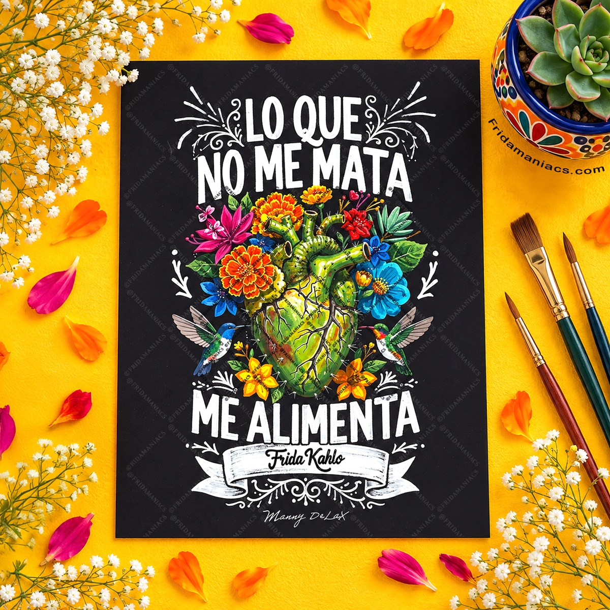 A rectangular black art print featuring a colorful illustrated heart and flowers with the Spanish text 'LO QUE NO ME MATA ME ALIMENTA' and 'Frida Kahlo' on a bright yellow background. The print is styled in a flat lay with paintbrushes, a succulent, white flowers, and orange petals.
