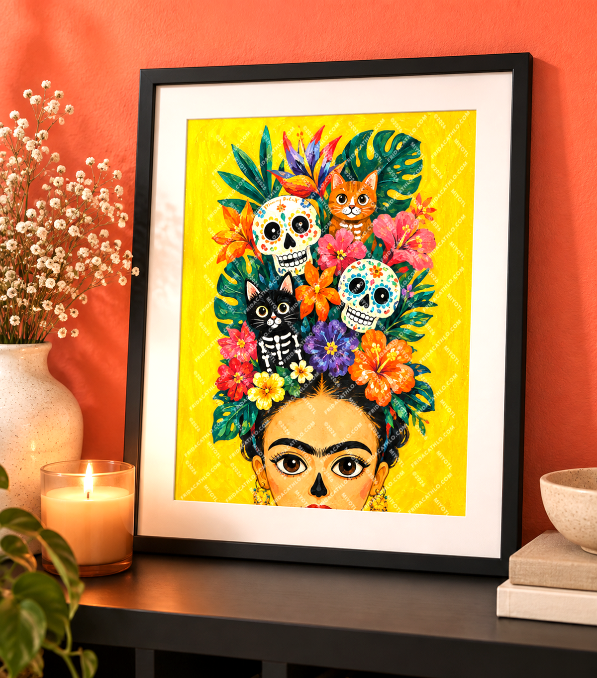 A framed art print featuring a colorful Day of the Dead style illustration with floral hair, sugar skulls, a black cat, and a face peeking out, displayed on a shelf against a terracotta wall with decorative plants and a candle.