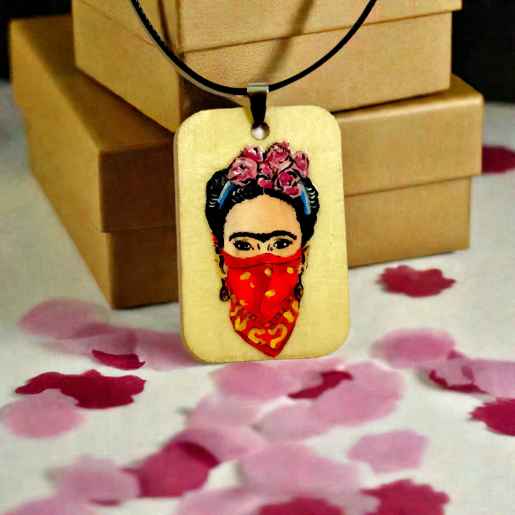 Frida-inspired necklace with a rectangular pendant depicting a woman wearing pink flowers and a red bandana, suspended from a black cord.