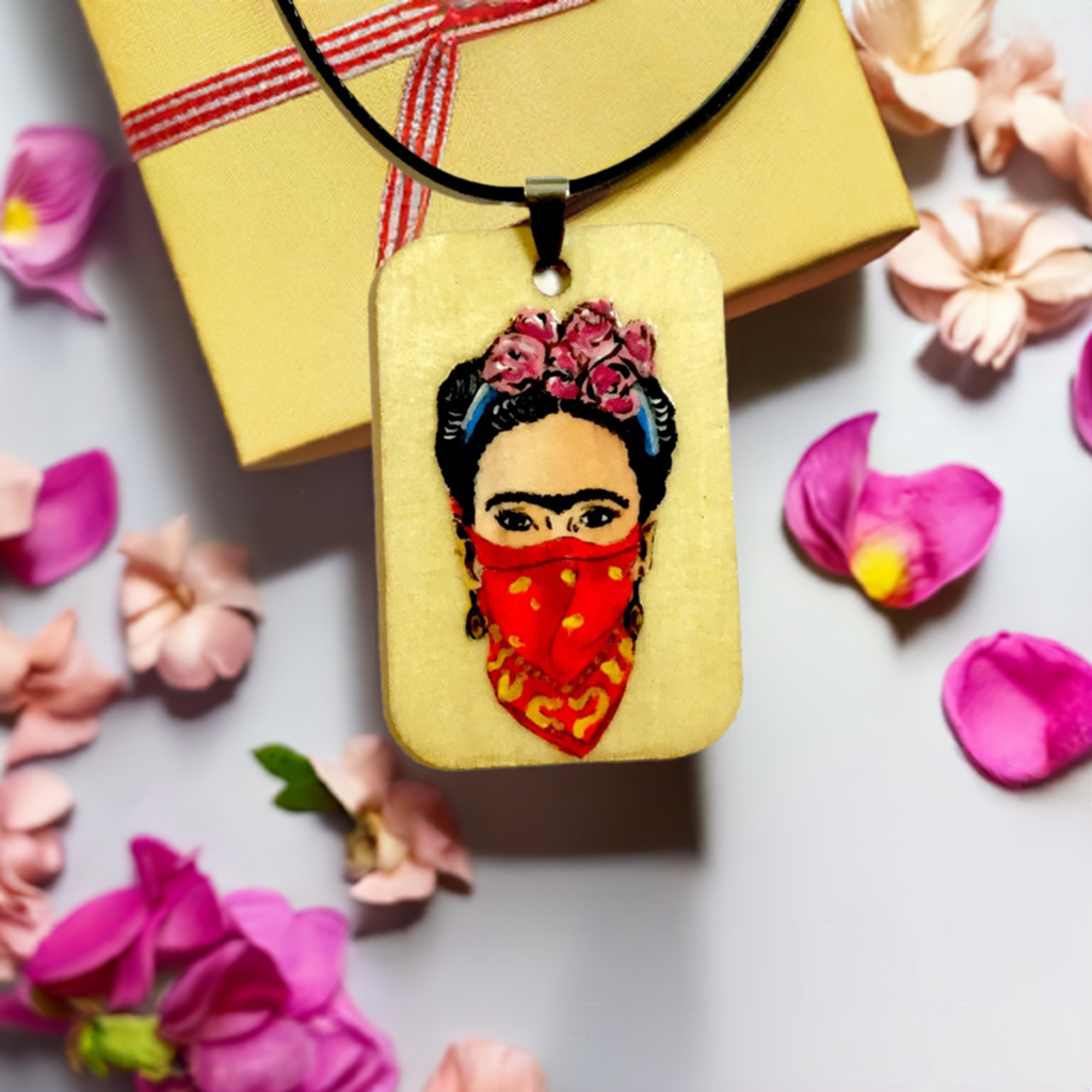 Frida-inspired necklace with a rectangular pendant depicting a woman wearing pink flowers and a red bandana, suspended from a black cord.