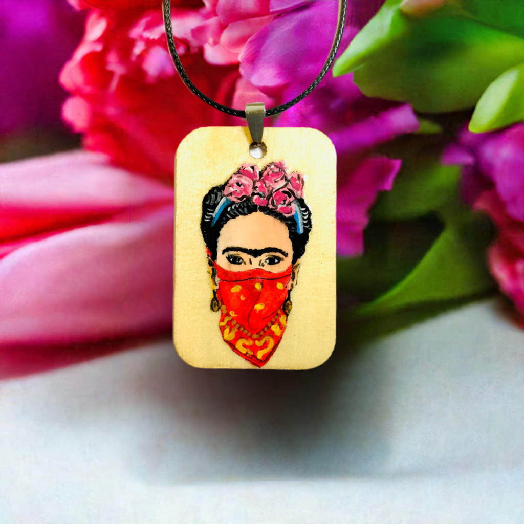 Frida-inspired necklace with a rectangular pendant depicting a woman wearing pink flowers and a red bandana, suspended from a black cord.