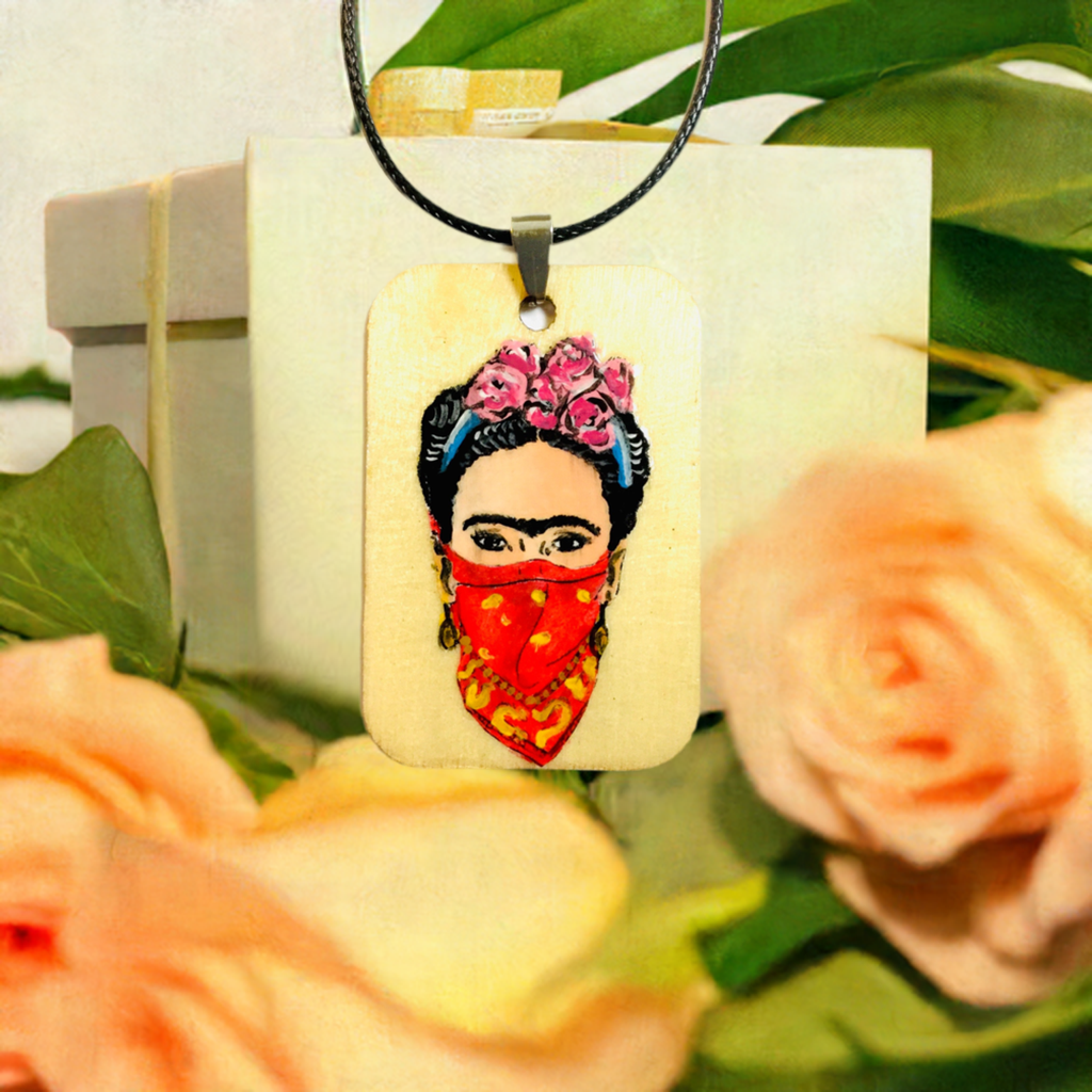 Frida-inspired necklace with a rectangular pendant depicting a woman wearing pink flowers and a red bandana, suspended from a black cord.