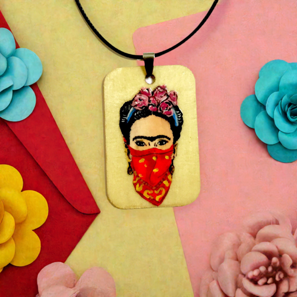 Frida-inspired necklace with a rectangular pendant depicting a woman wearing pink flowers and a red bandana, suspended from a black cord.
