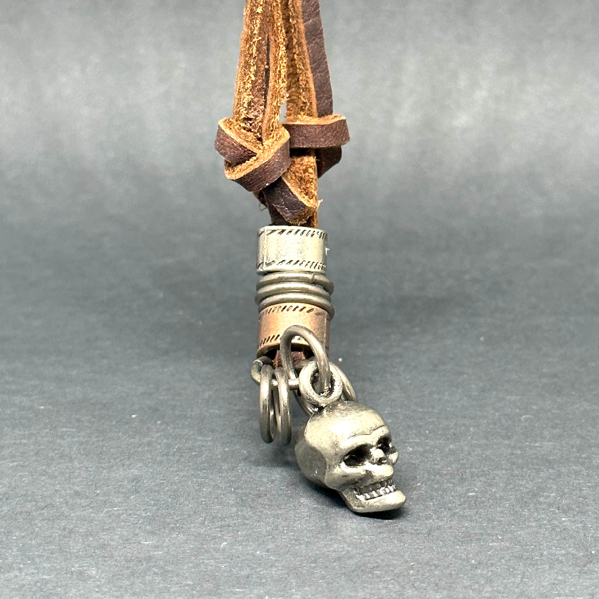 Metallic skull pendant charm with stainless stain rings and disk. Brown leather necklace cord for guys.