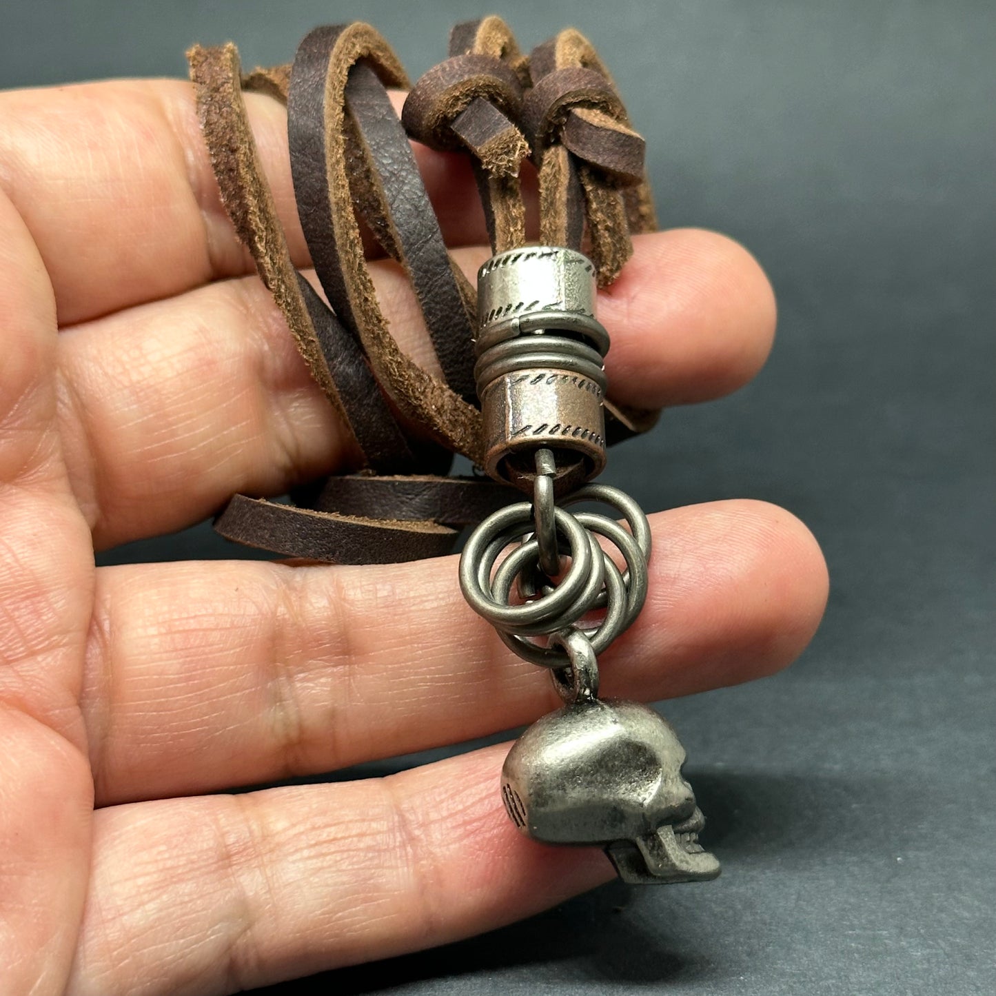 Metallic skull pendant charm with stainless stain rings and disk. Brown leather necklace cord for guys.