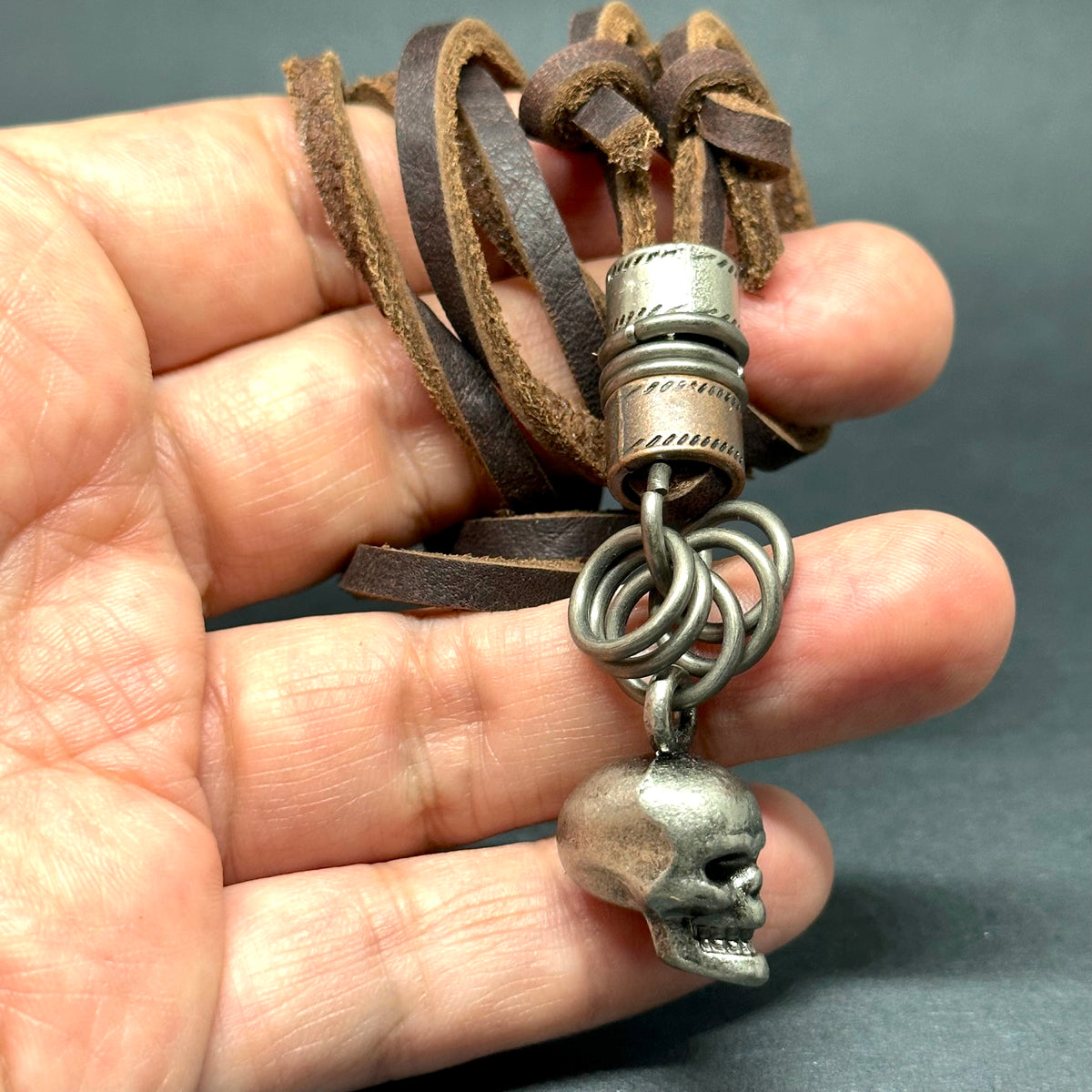 Metallic skull pendant charm with stainless stain rings and disk. Brown leather necklace cord for guys.