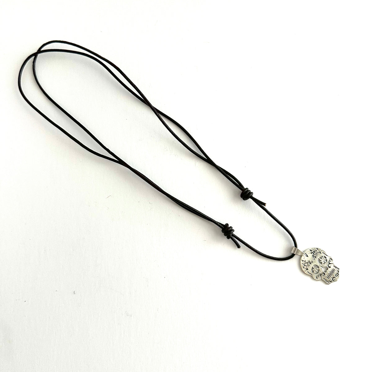 Full brown leather necklace laid out on white, showing the long cord loop, two sliding knots, and silver-tone skull pendant.