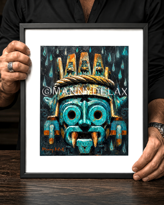A framed art print featuring a stylized turquoise and gold Aztec-inspired mask, held by a person wearing a black shirt over a dark wooden table.
