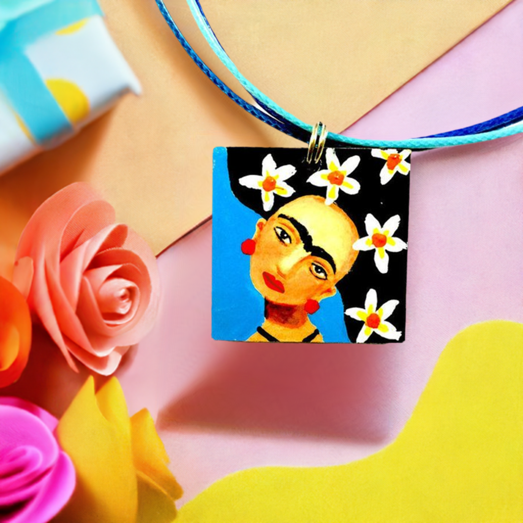 Hand painted Frida Kahlo inspired pendant with blue and white-yellow-orange wilds flowers on hair. Mexican artist portrait art to wear for women and girls. Unique gift idea for fridamaniacs, fridalovers, and frida fans.