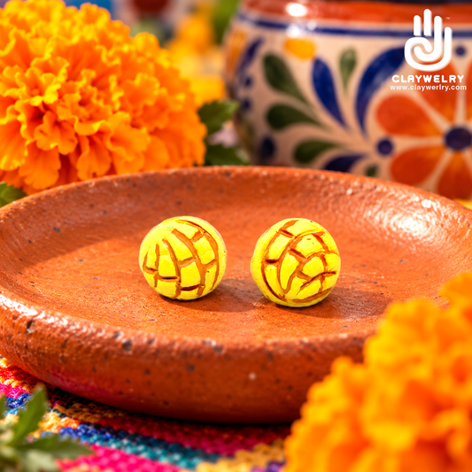 Yellow concha clay stud earrings on a terracotta plate with orange marigolds and painted pottery behind.
